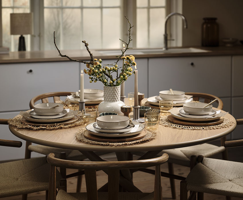 Round dining table set for a birthday dinner with vase, plates, bowls, glasses and candles 